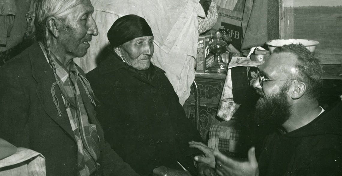 Black-and-white photo of a Capuchin friar speaking with a Northern Cheyenne family.